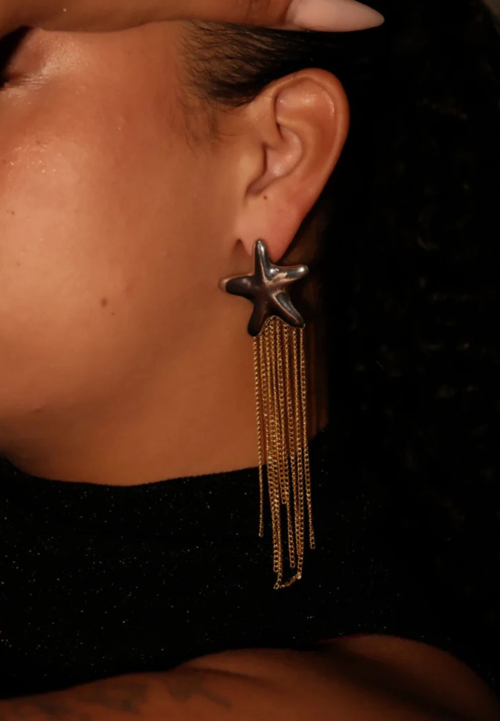 Silver star stud earring with cascading gold-plated chains, worn on an ear.