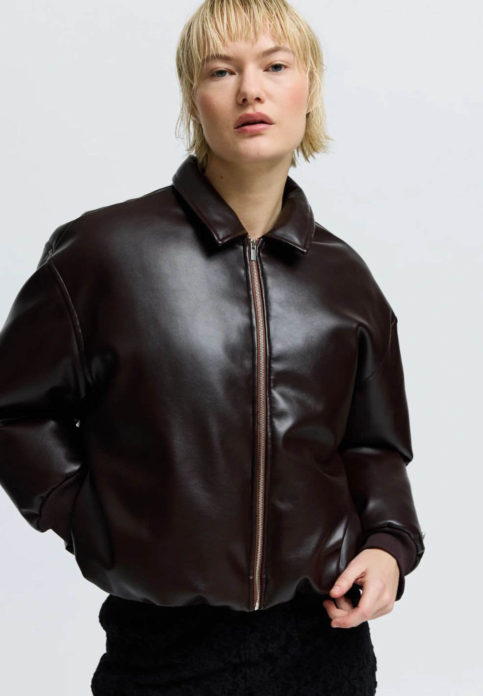 Person wearing a brown leather jacket on a light gray background