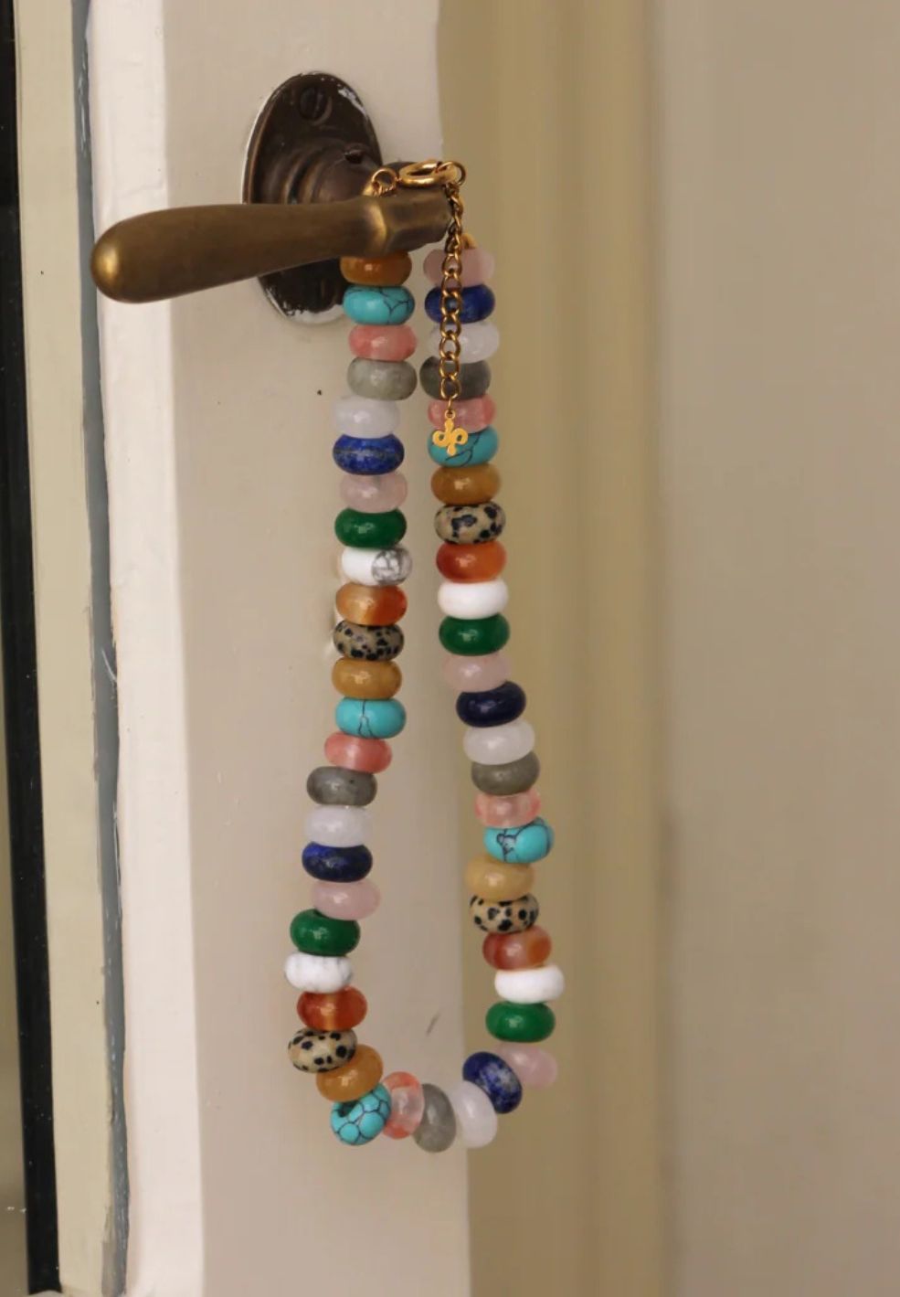 Vibrant natural stone necklace with eclectic colorful beads and 18K gold-plated details, hanging from a brass door handle.
