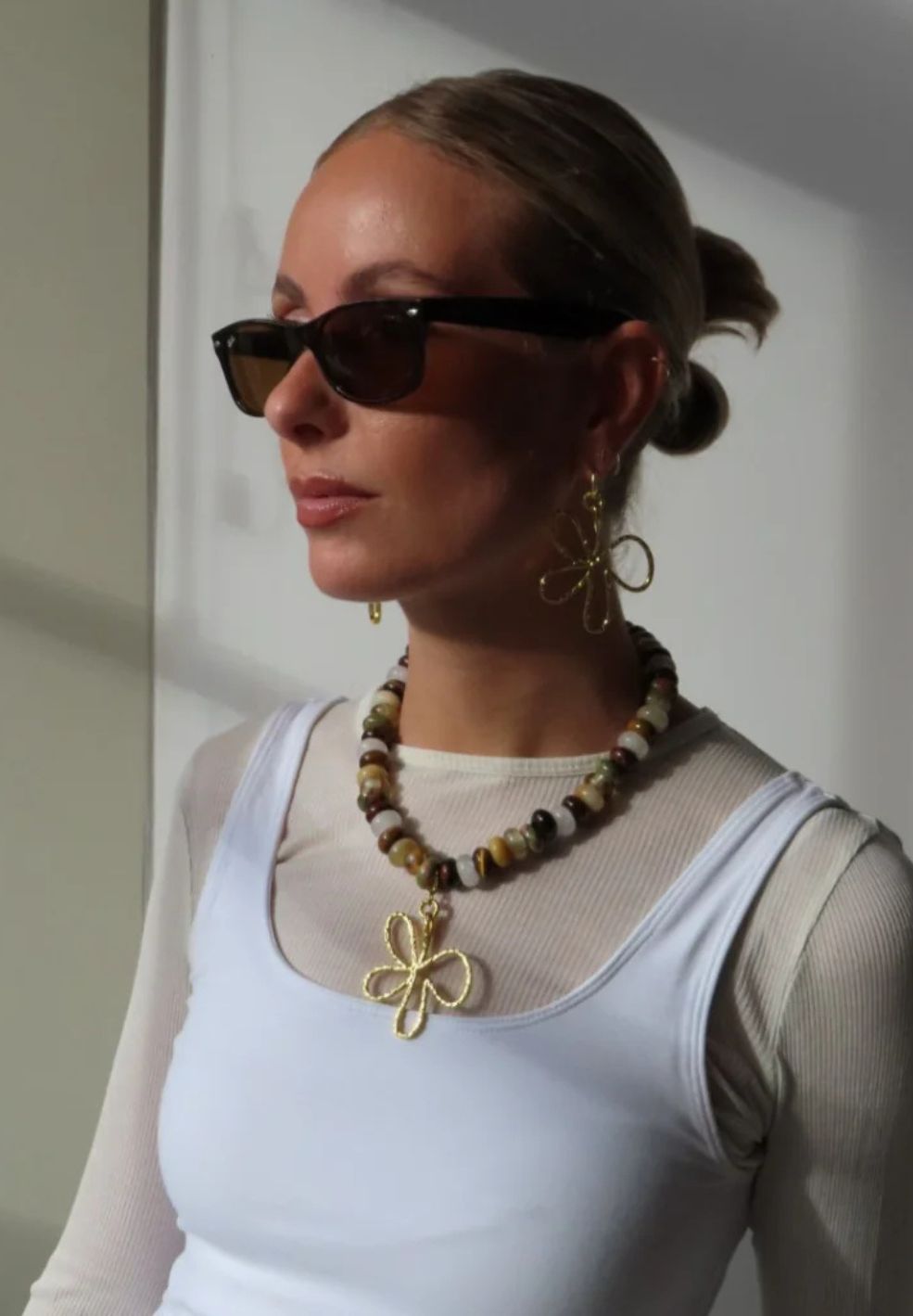 Woman wearing a natural stone necklace with a gold-plated flower pendant and matching earrings.
